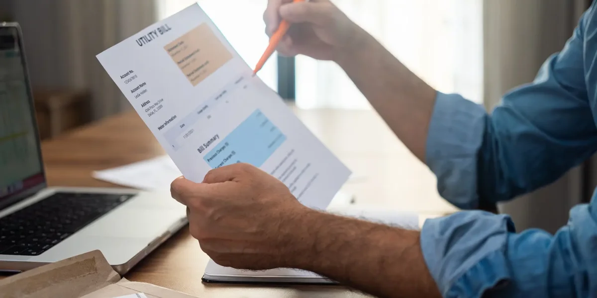 Businessman with pen checks utility bill debt sitting at desk with laptop payments regulation